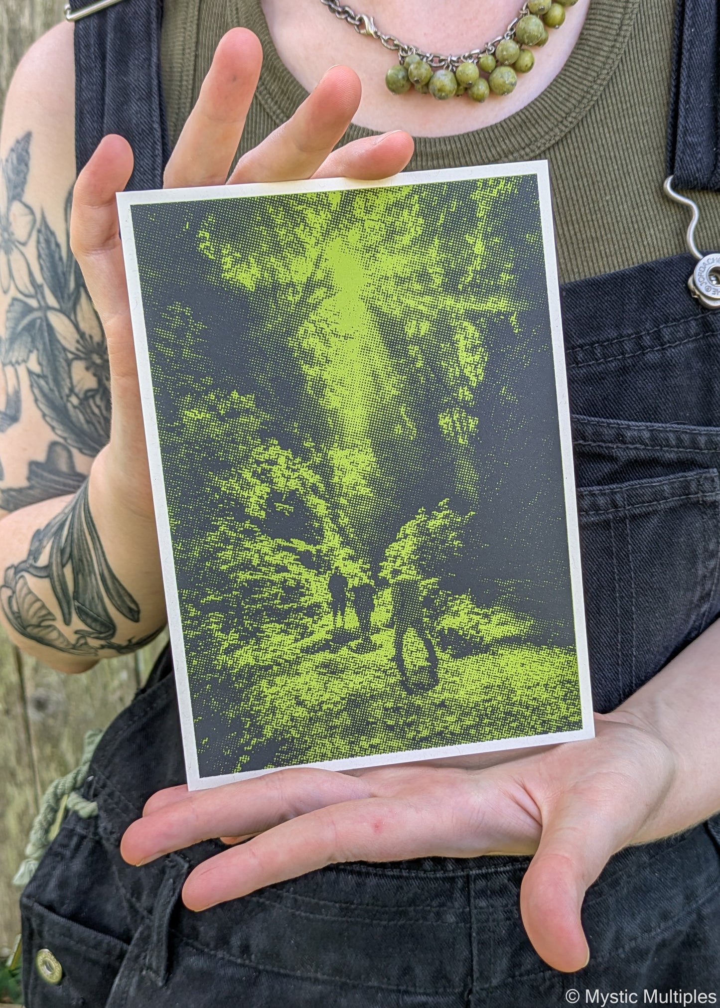 A person holding the Fern Valley postcard in green and black