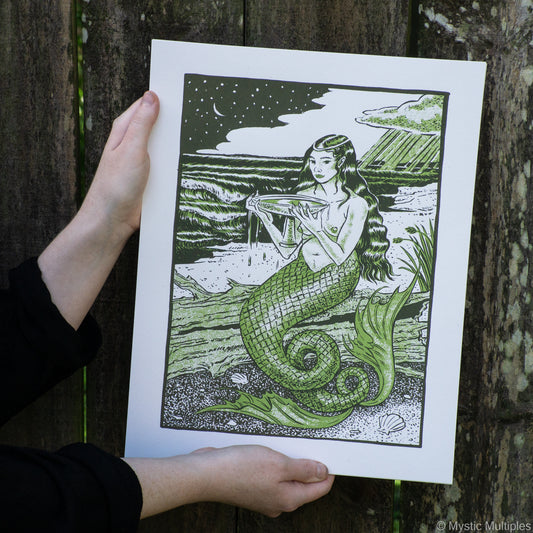 The queen of cups as a mermaid on the shore, holding a cup