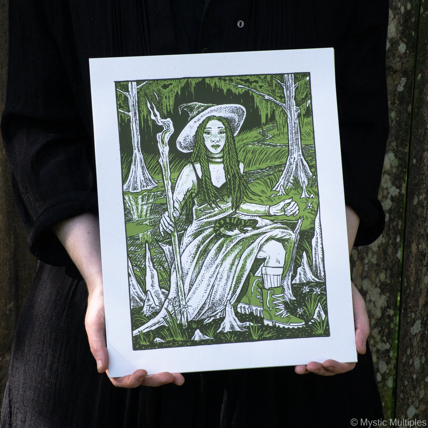 The queen of wands sitting in a swamp with her companion fire salamander on her lap
