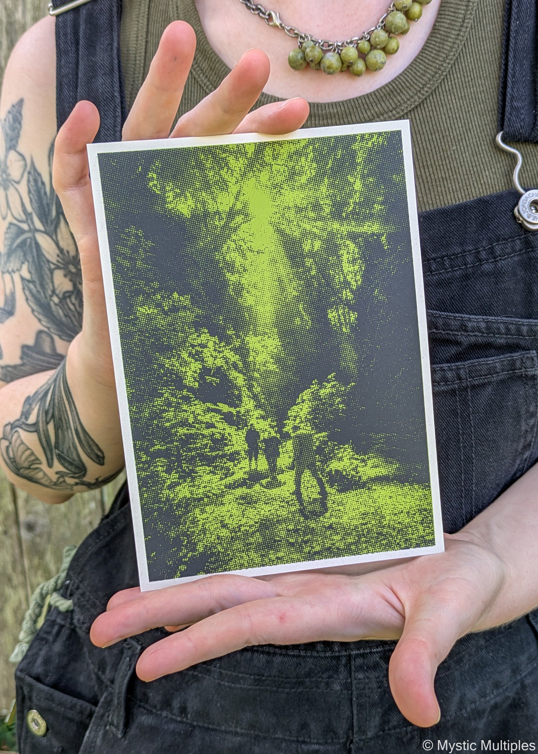 A person holding the Fern Valley postcard in green and black