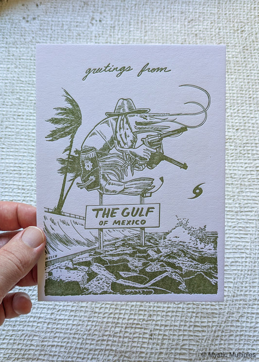 Hand holding a card with a green and white illustration of a pistol packing shrimp and 'Gulf of Mexico' sign.