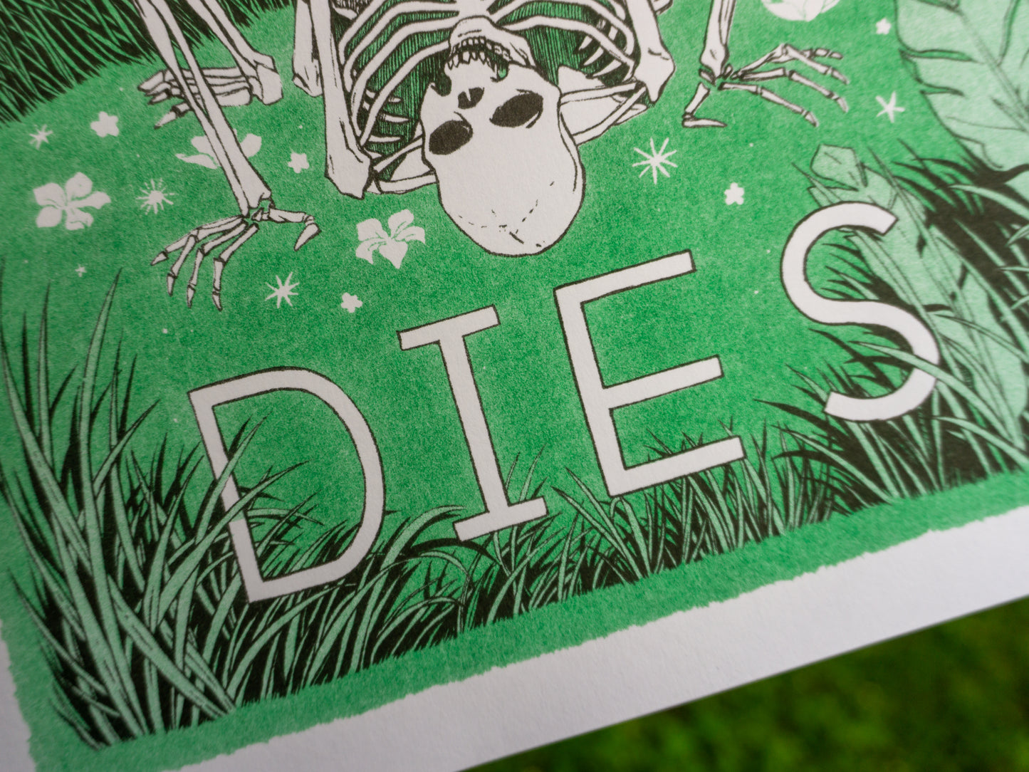 Close up of the word DIES from the Love Never Dies riso poster. Green and black inks show grass around the letters, and a skeleton in the background.
