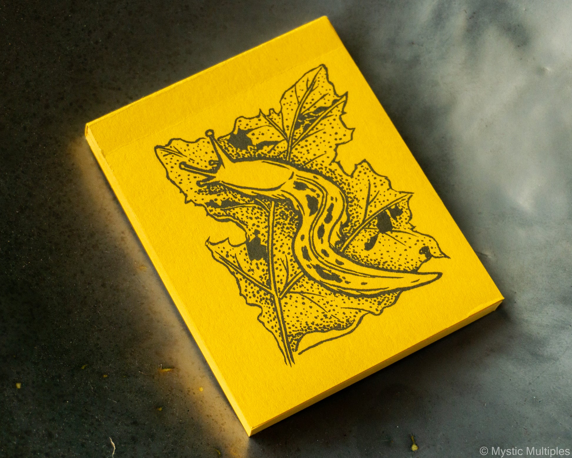 Yellow notebook with black leaf banana slug design on a dark surface