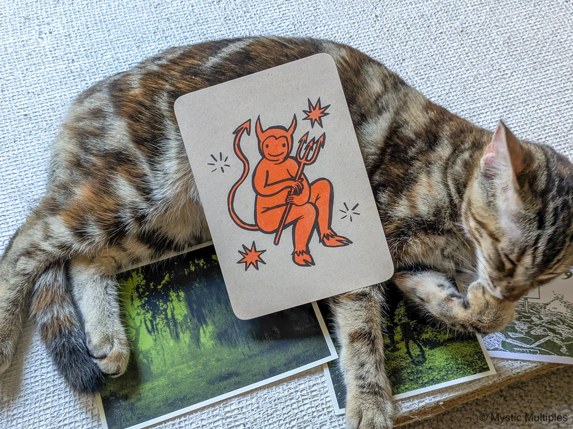 Tiny devil card on top of a cat who is also on top of more cards